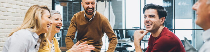 Frauen und Männer sitzen lachend zusammen in einem Bürozimmer